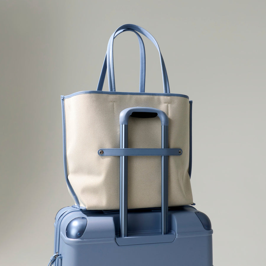 Beige tote bag on top of a blue suitcase against a plain background